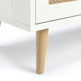 [White] Rattan TV Unit detail showing rattan door, white wood frame, base trim, and tapered solid wood leg on a soft floor