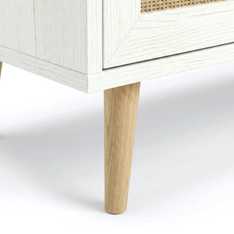 [White] Rattan TV Unit detail showing rattan door, white wood frame, base trim, and tapered solid wood leg on a soft floor
