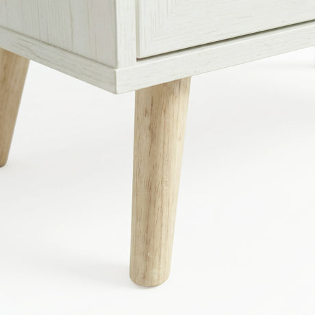 [White] Wovena close-up of a solid tapered natural wood leg where it meets the whitewashed cabinet base, showing two legs and the cabinet corner edge