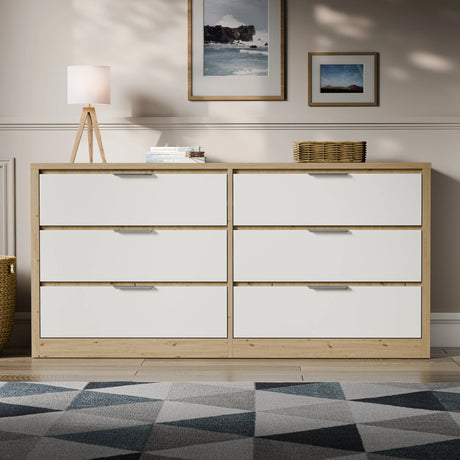 Wide chest of drawers with 6 drawers and metallic handles in oak white finish, placed against a wall in a modern room