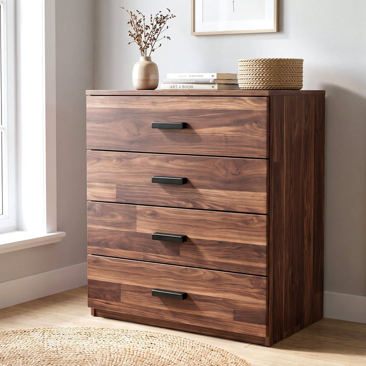 [Dark Bronx] A four-drawer wooden chest of drawers with a warm medium-brown finish and black metal handles, styled in a bright room next to a window with books and decorative items on top.