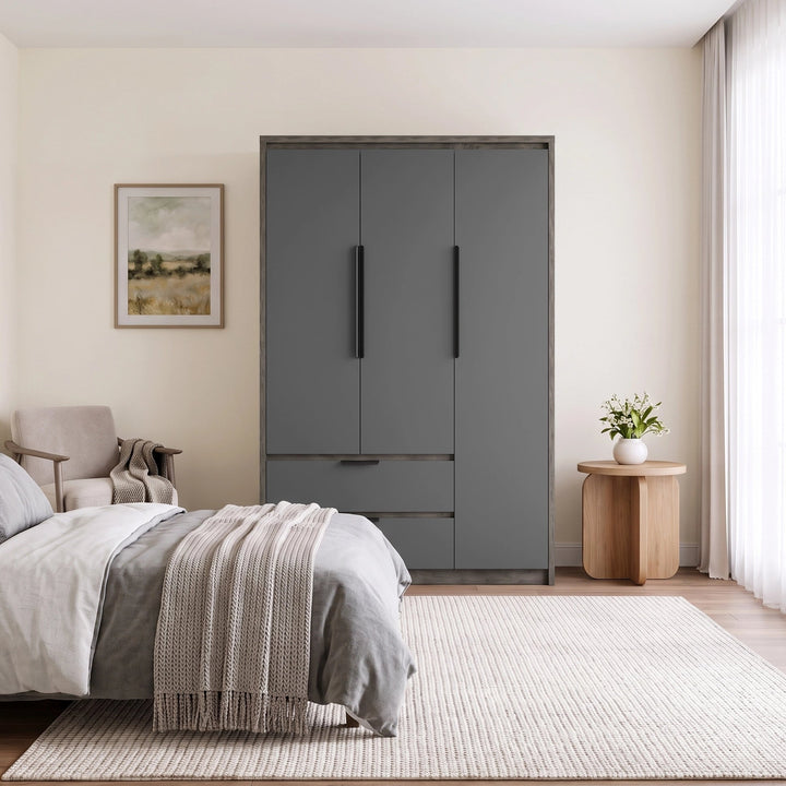 [Wooden Grey] A modern bedroom scene featuring a tall gray three-door wardrobe with two long black handles and a lower drawer, set against cream walls next to a bed and a small wooden side table.