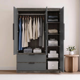 [Wooden Grey] three-door wardrobe with open doors, shown in a styled bedroom setting. The wardrobe is filled with folded and hanging clothes, and sits next to a small wooden side table with a white vase of flowers.