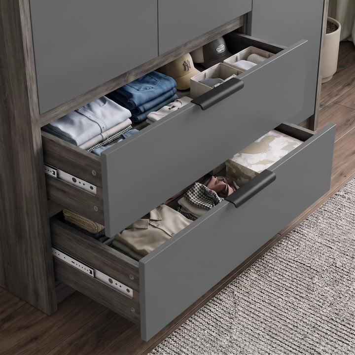 [Wooden Grey] wardrobe with drawers with dark handles, shown partially open to reveal neatly folded clothing and storage bins inside, in a real bedroom setting with wood flooring and a rug.