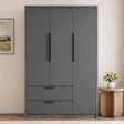 [Wooden Grey] three-door wardrobe with a matte dark gray finish and a rustic weathered wood frame, shown in a styled room setting next to a wooden side table with a vase of flowers.