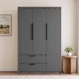 [Wooden Grey] three-door wardrobe with a matte dark gray finish and a rustic weathered wood frame, shown in a styled room setting next to a wooden side table with a vase of flowers.