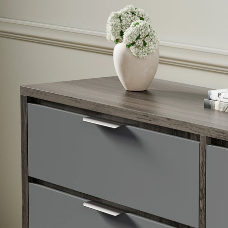 Wooden-Grey finish chest of drawers with metallic handles, shown in a bright room setting with a decorative vase on top