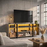 [Wooden Grey] Industrial LED TV Stand with Storage styled in a concrete-walled living room with warm amber LED underlighting, open shelves holding a soundbar, books and a basket