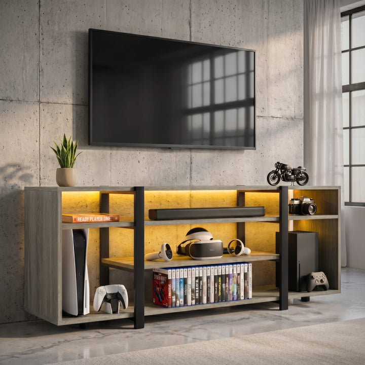 [Wooden Grey] Zelumi TV stand angled view in a concrete-wall room with warm yellow LED shelves, consoles, VR headset, game cases and plant on top surface