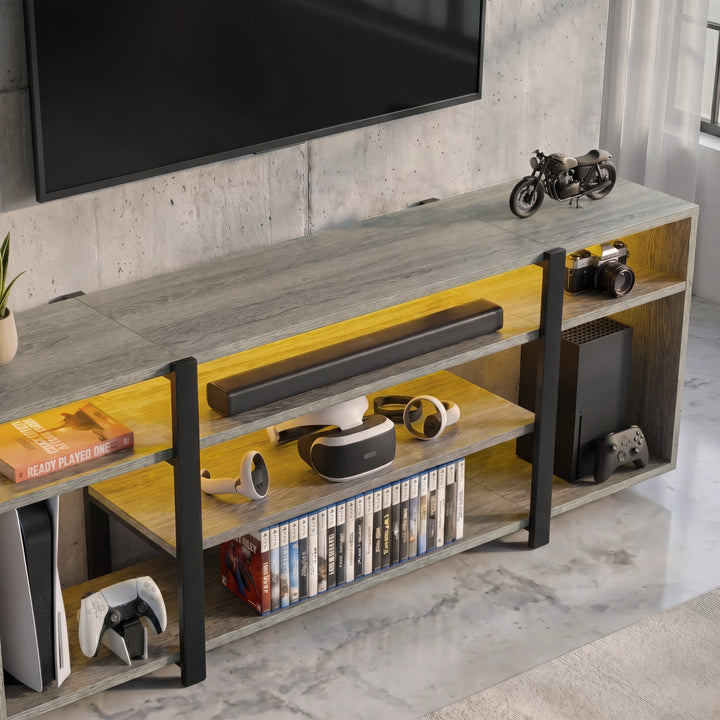 [Wooden Grey] Zelumi TV stand overhead close-up showing grey wood top surface, warm LED-lit shelves with VR headset, soundbar, console and game cases