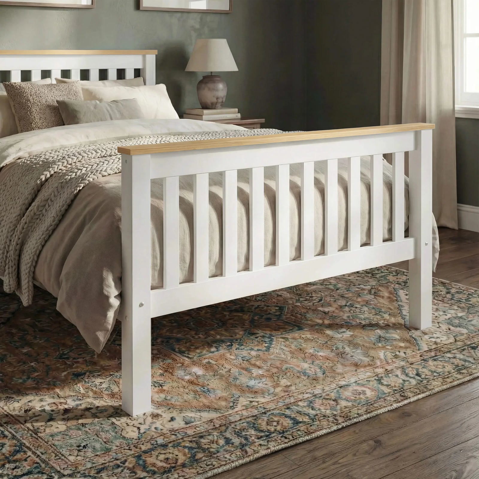 [Single | White + Pine] A white wooden bed frame with a light natural wood footboard rail, shown in a styled bedroom setting with beige bedding, a patterned rug, and a nightstand.