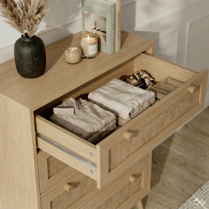 [Oak] Wovena chest top drawer pulled open in a styled room, showing folded clothing inside with candles and books on top