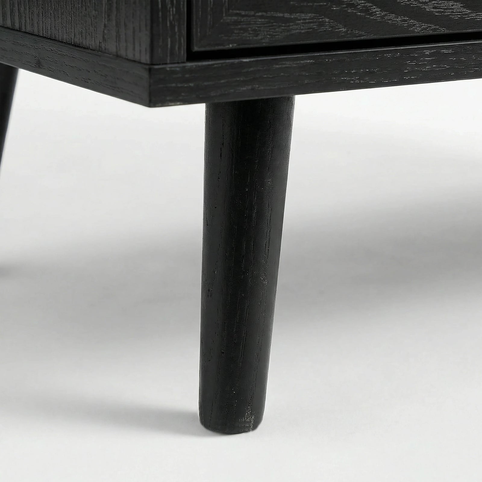 [Black] Detail of Wovena rattan bedside angled leg attached to cabinet, dark grain on leg and body