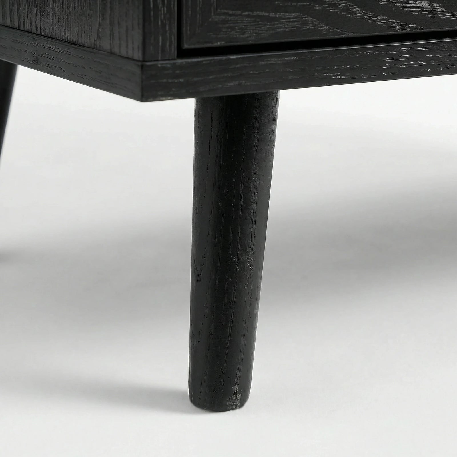 [Black] Detail of Wovena rattan bedside angled leg attached to cabinet, dark grain on leg and body