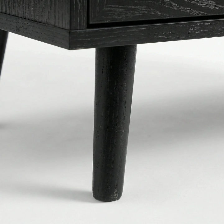 [Black] Detail of Wovena rattan bedside angled leg attached to cabinet, dark grain on leg and body