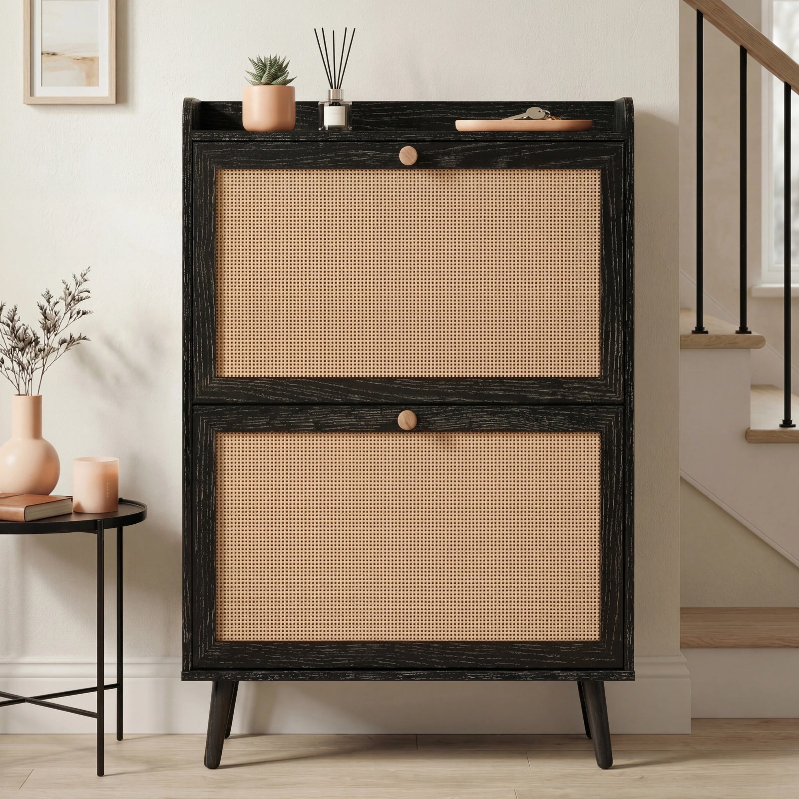 [Black] Wovena Rattan Black 2 Door Shoe Storage Cabinet front-facing in neutral hallway with black balustrade staircase and round black side table alongside