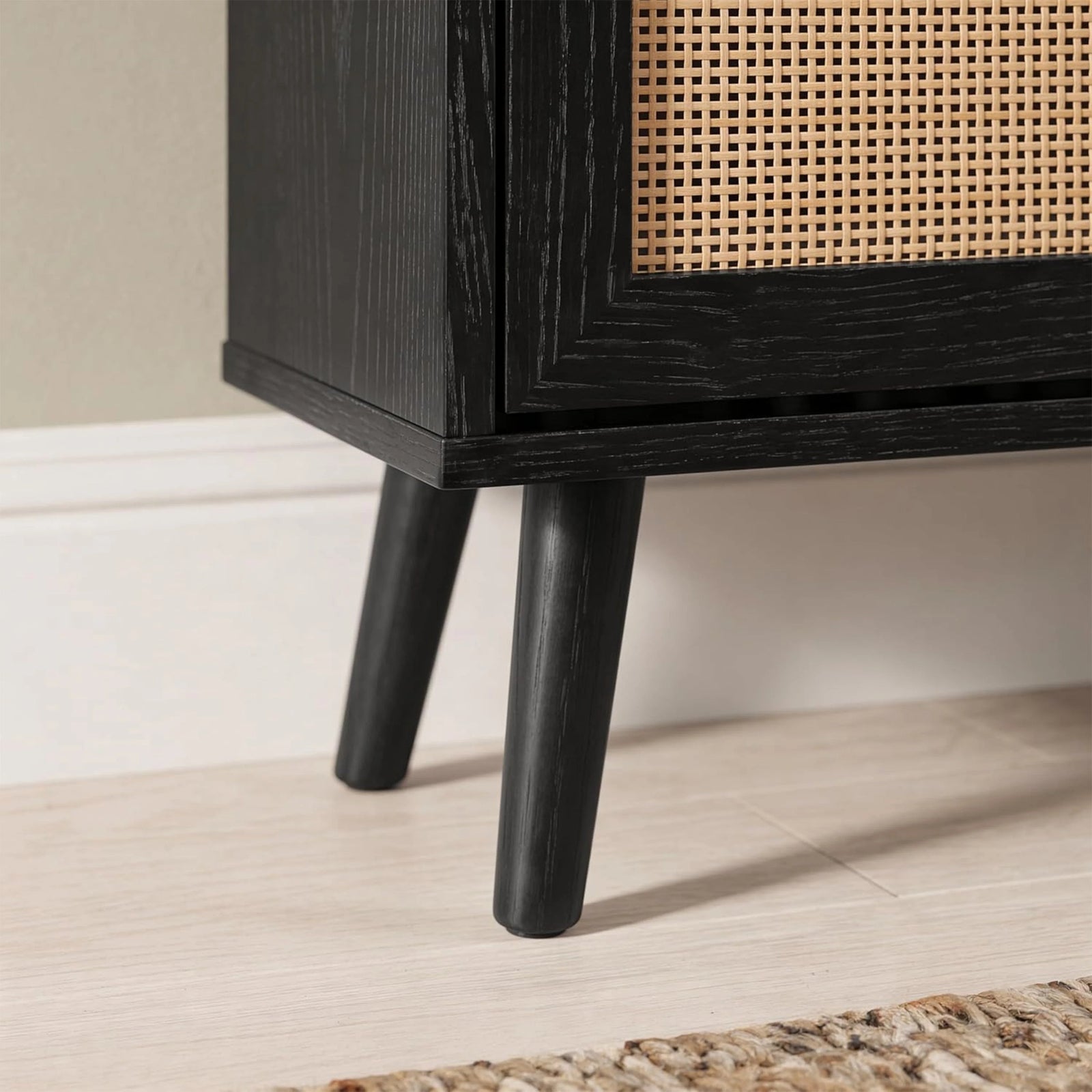 [Black] Wovena Rattan Black 2 Door Shoe Storage Cabinet base close-up showing tapered black legs on light tile floor with black grain cabinet body and rattan door panel