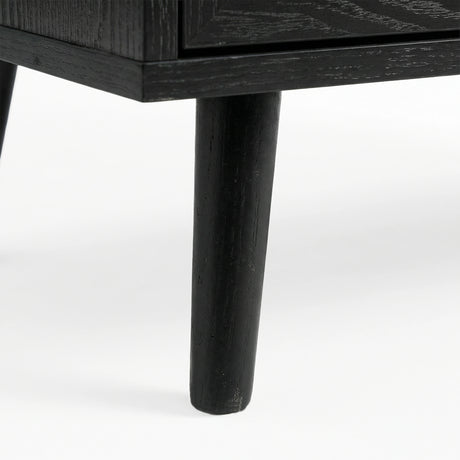 [Black] Close-up of black-painted tapered leg supporting Wovena rattan chest, wood grain visible through finish