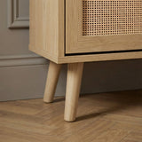 [Oak] Wovena Rattan Oak 2 Door Shoe Storage Cabinet base close-up showing tapered natural oak legs on herringbone floor with oak grain cabinet body and rattan door panel