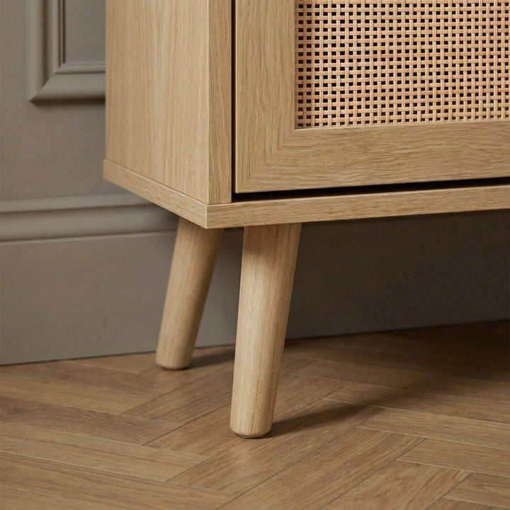 [Oak] Wovena Rattan Oak 2 Door Shoe Storage Cabinet base close-up showing tapered natural oak legs on herringbone floor with oak grain cabinet body and rattan door panel