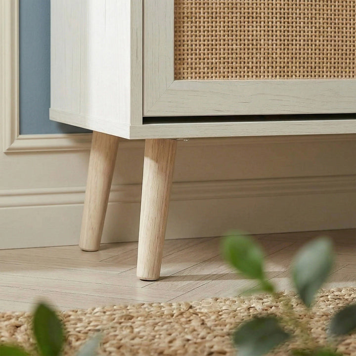 [White] Wovena Rattan White 2 Door Shoe Storage Cabinet base close-up showing tapered natural wood legs on herringbone floor with rattan door panel detail