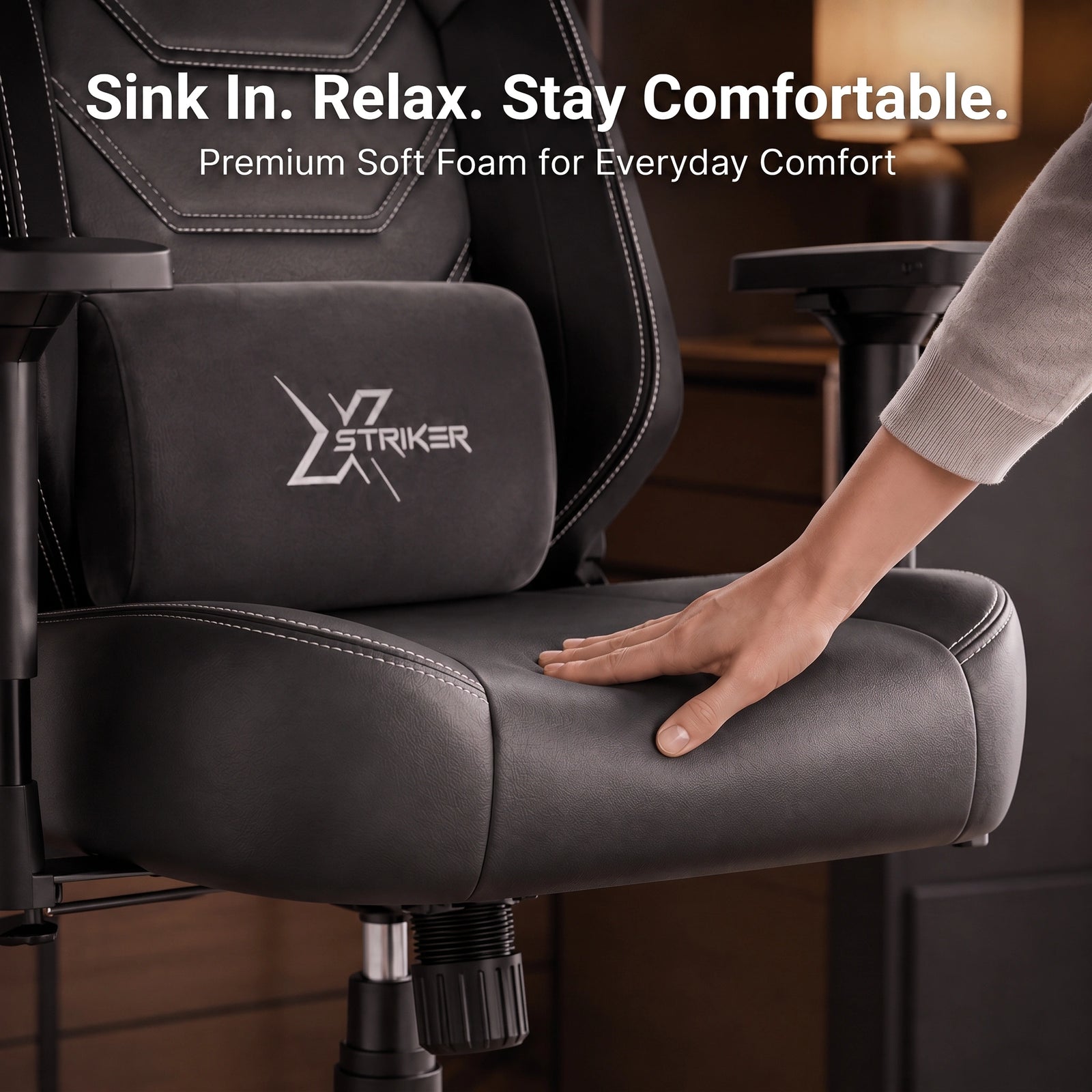 [Black] gaming chair with a matching lumbar support cushion featuring the 'XSTRIKER' logo. A person's hand is resting on the padded seat, demonstrating comfort.