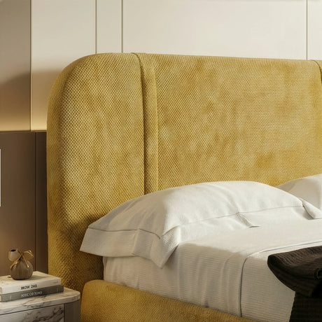 Close view of curved padded backrest in textured yellow upholstery of a double bed frame with a neutral bedding